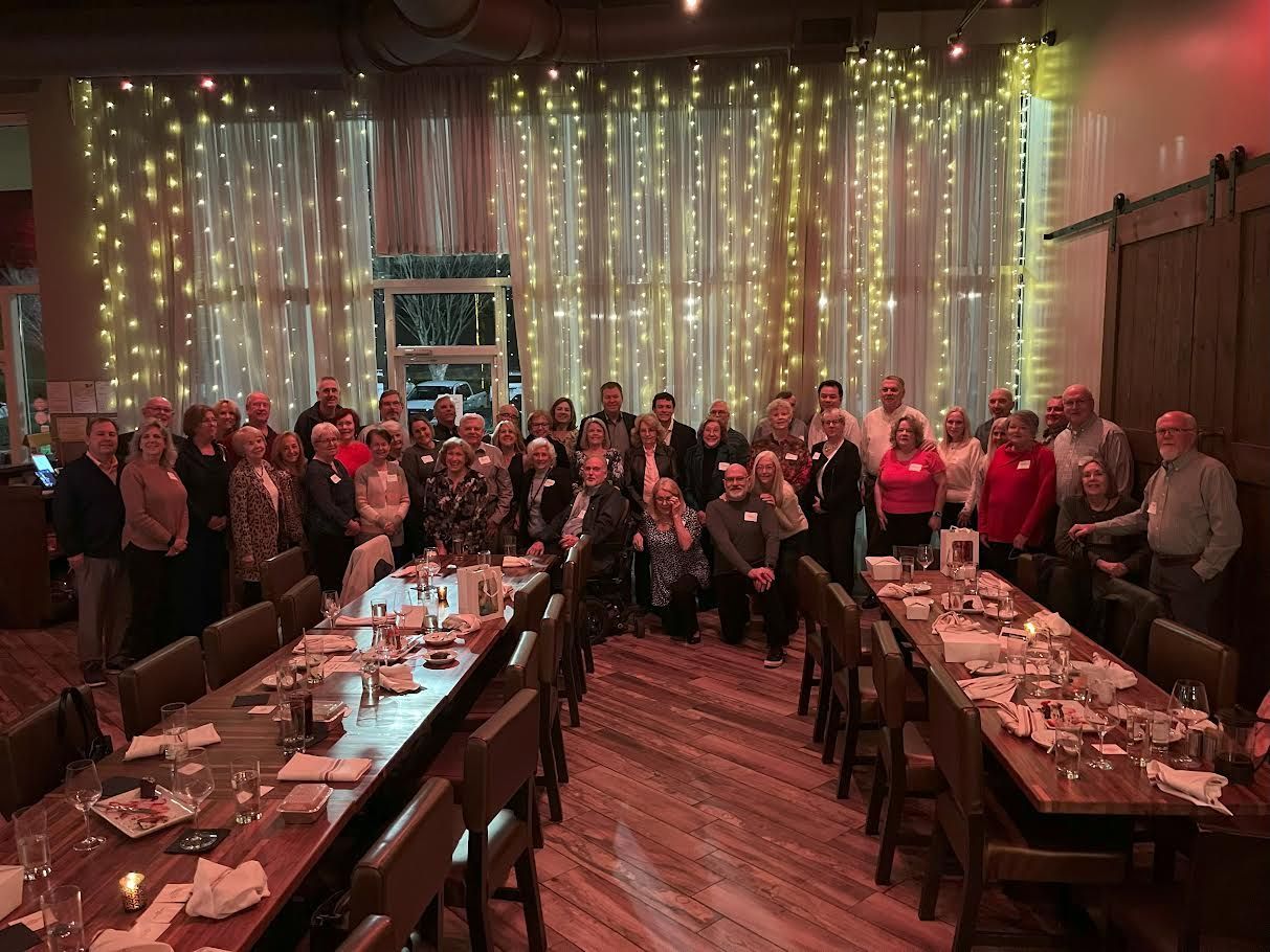 A group of people are standing around a long table in a restaurant.
