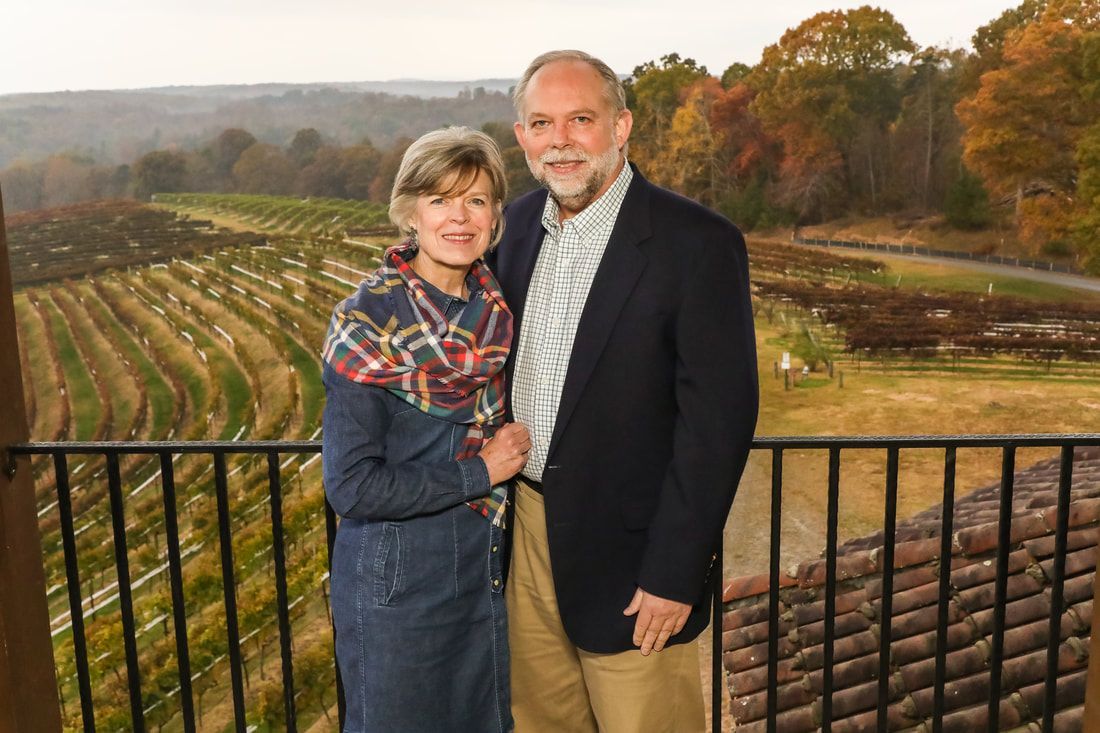 A man and a woman are standing next to each other on a balcony overlooking a vineyard.
