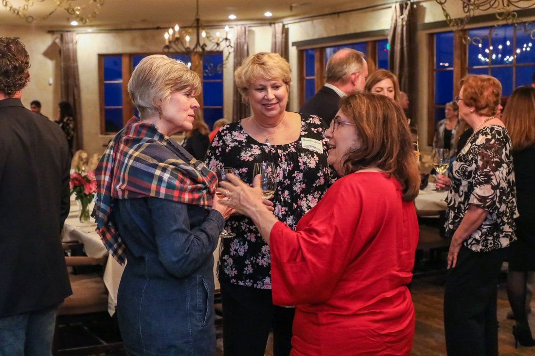 A group of women are standing in a room talking to each other.