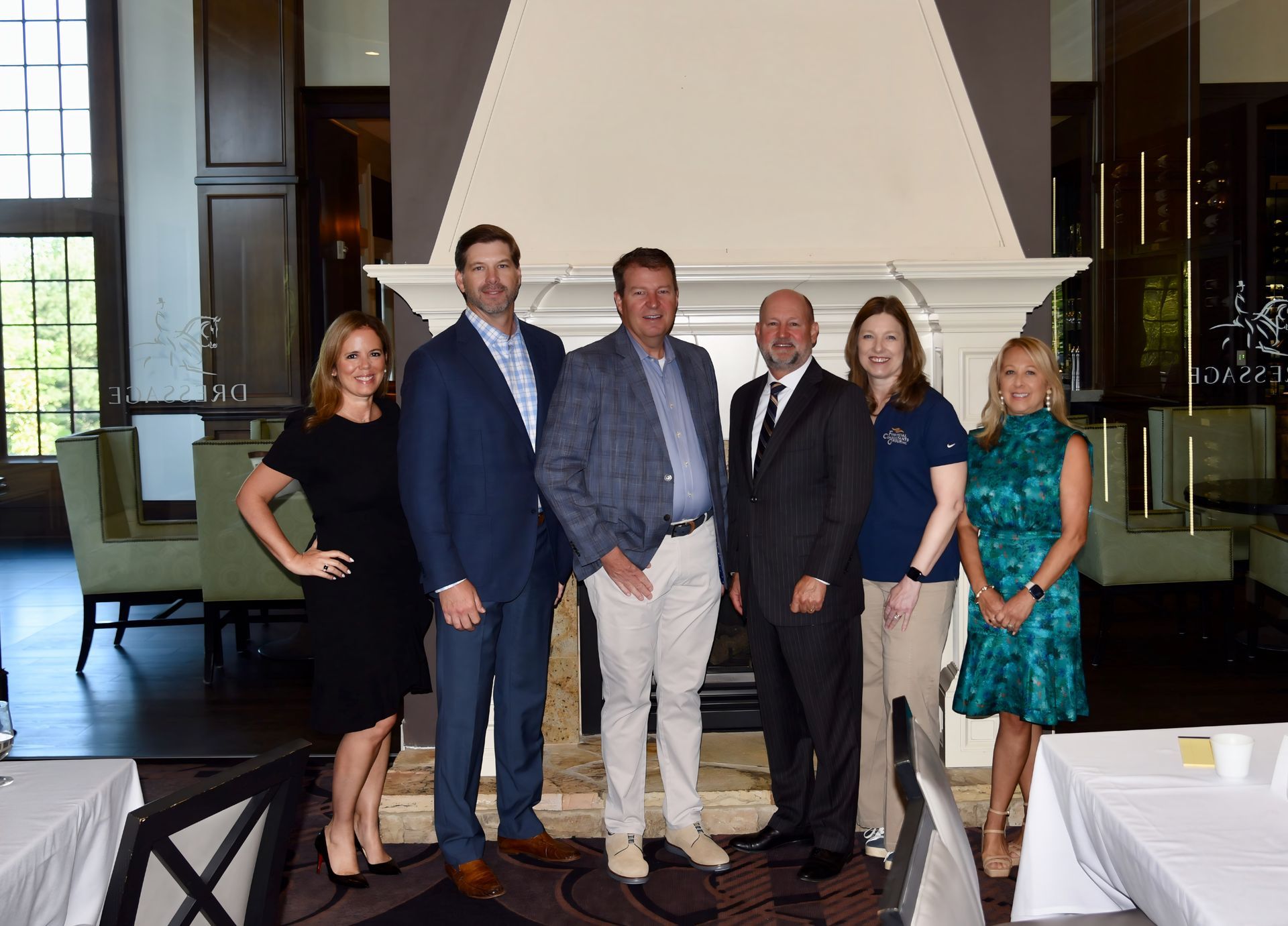 A group of seven people stand near a fireplace in a dining room. They smile and pose for a photo.