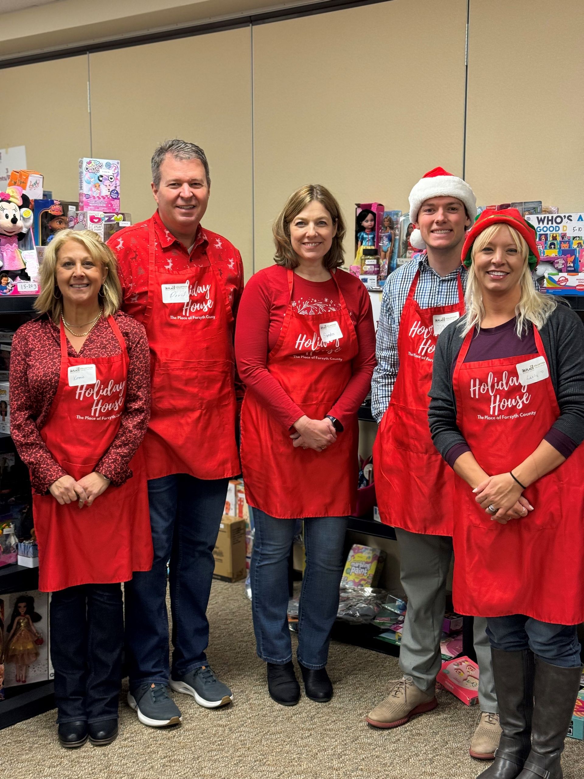A group of people wearing red aprons and santa hats are posing for a picture.