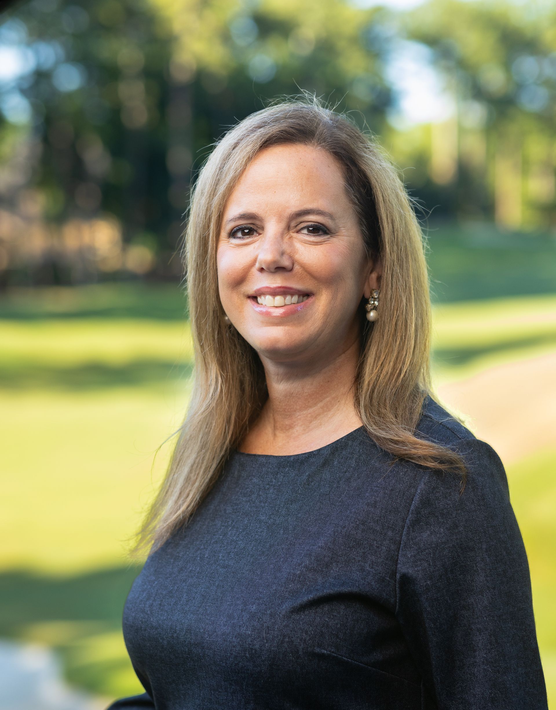 A woman in a black shirt is smiling in front of a brick wall.