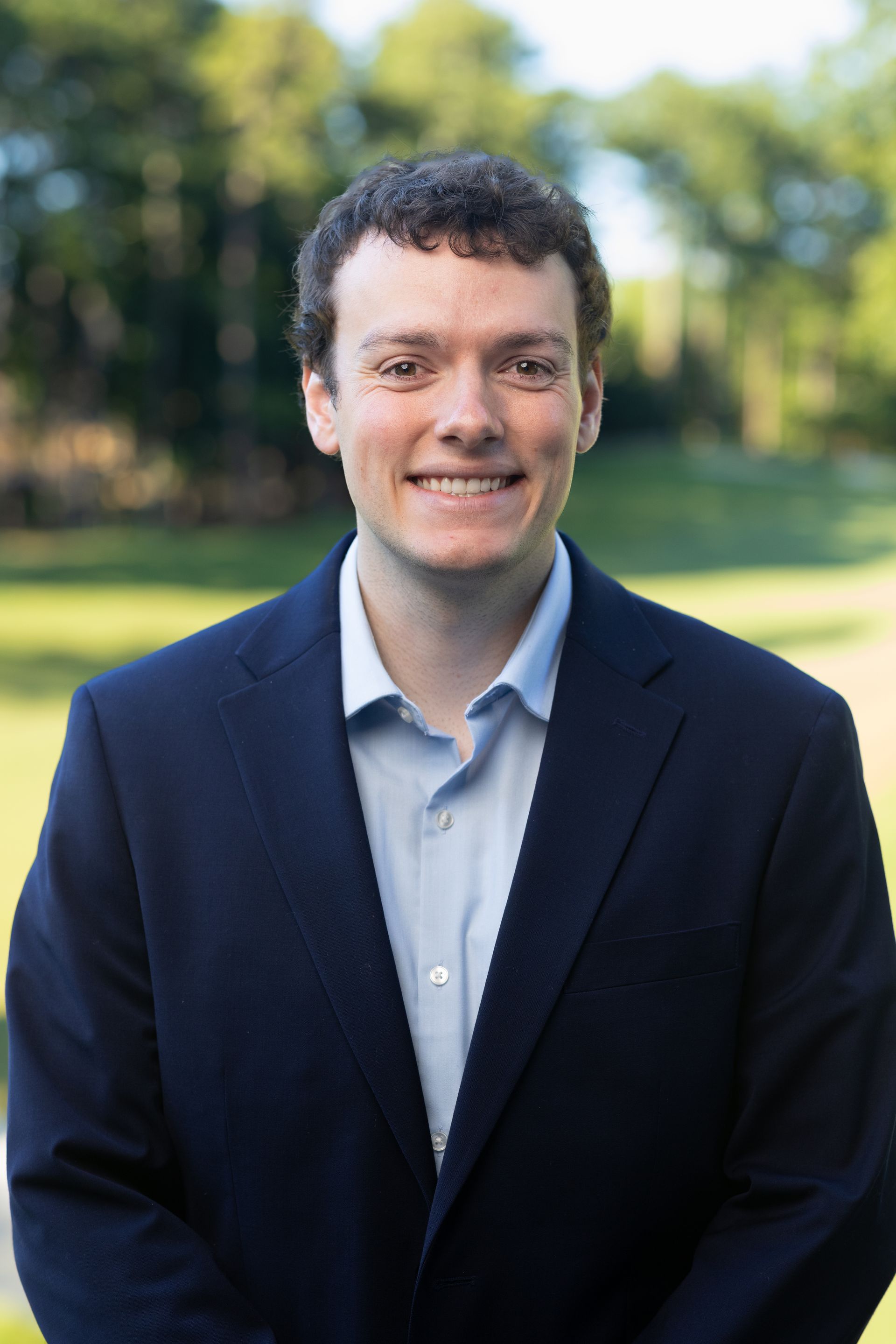 A man in a suit is smiling in front of a brick wall.