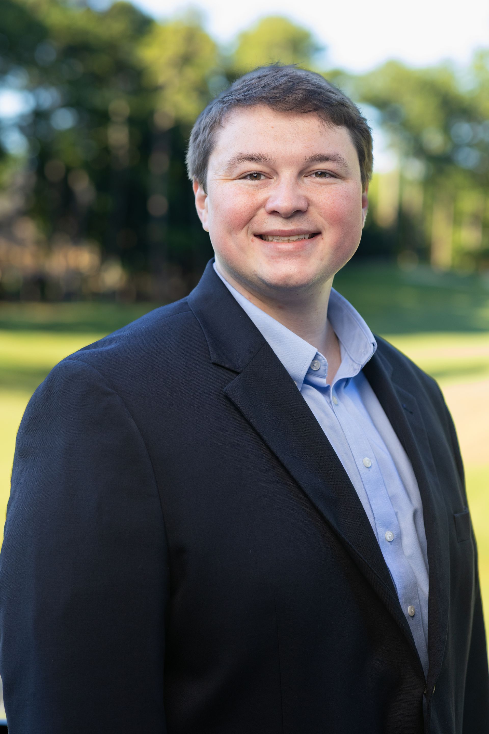 A young man in a plaid shirt is smiling in front of a brick wall.