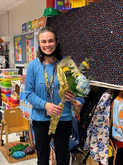 A woman is holding a bouquet of flowers in a classroom.
