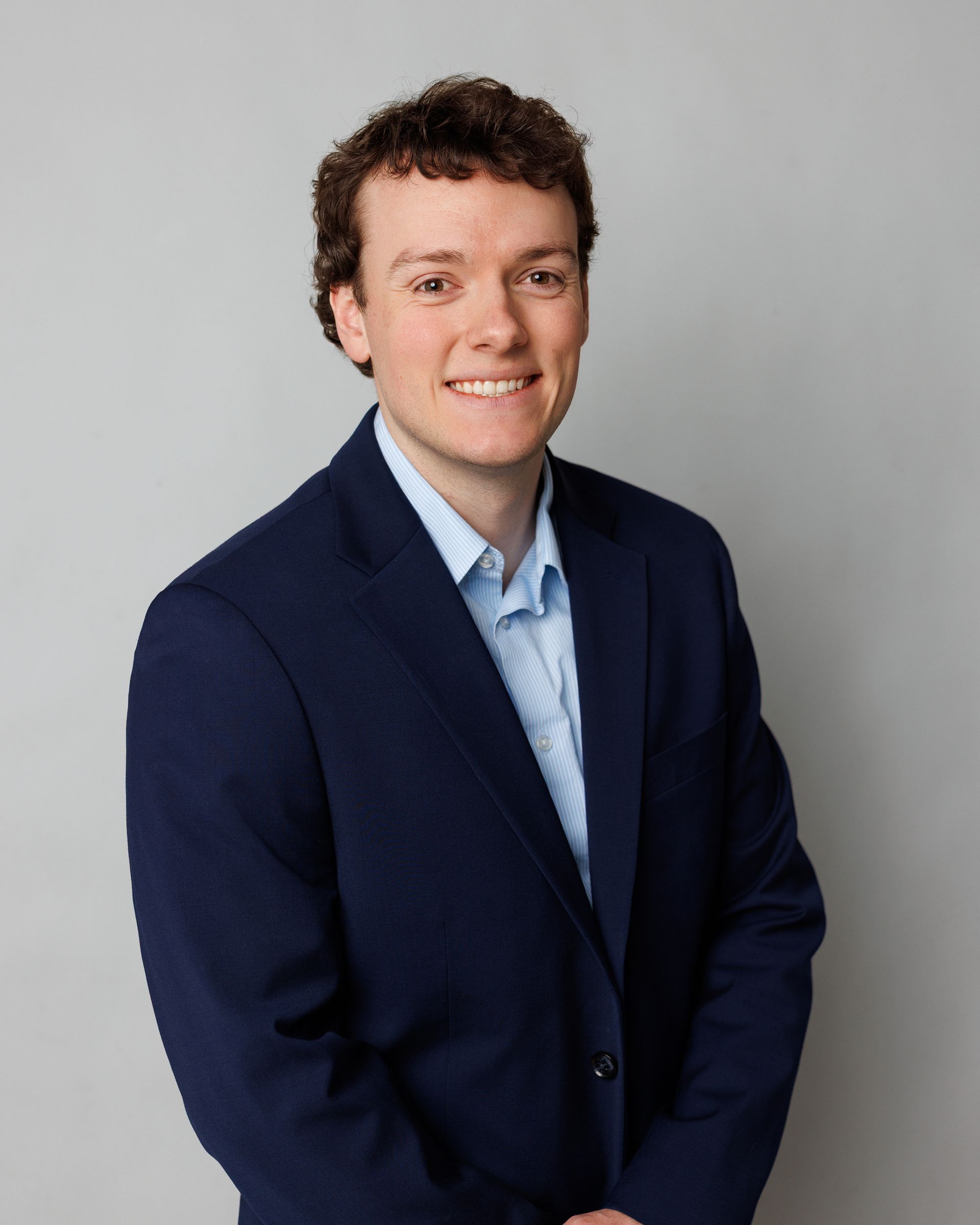 A man in a suit is smiling in front of a brick wall.
