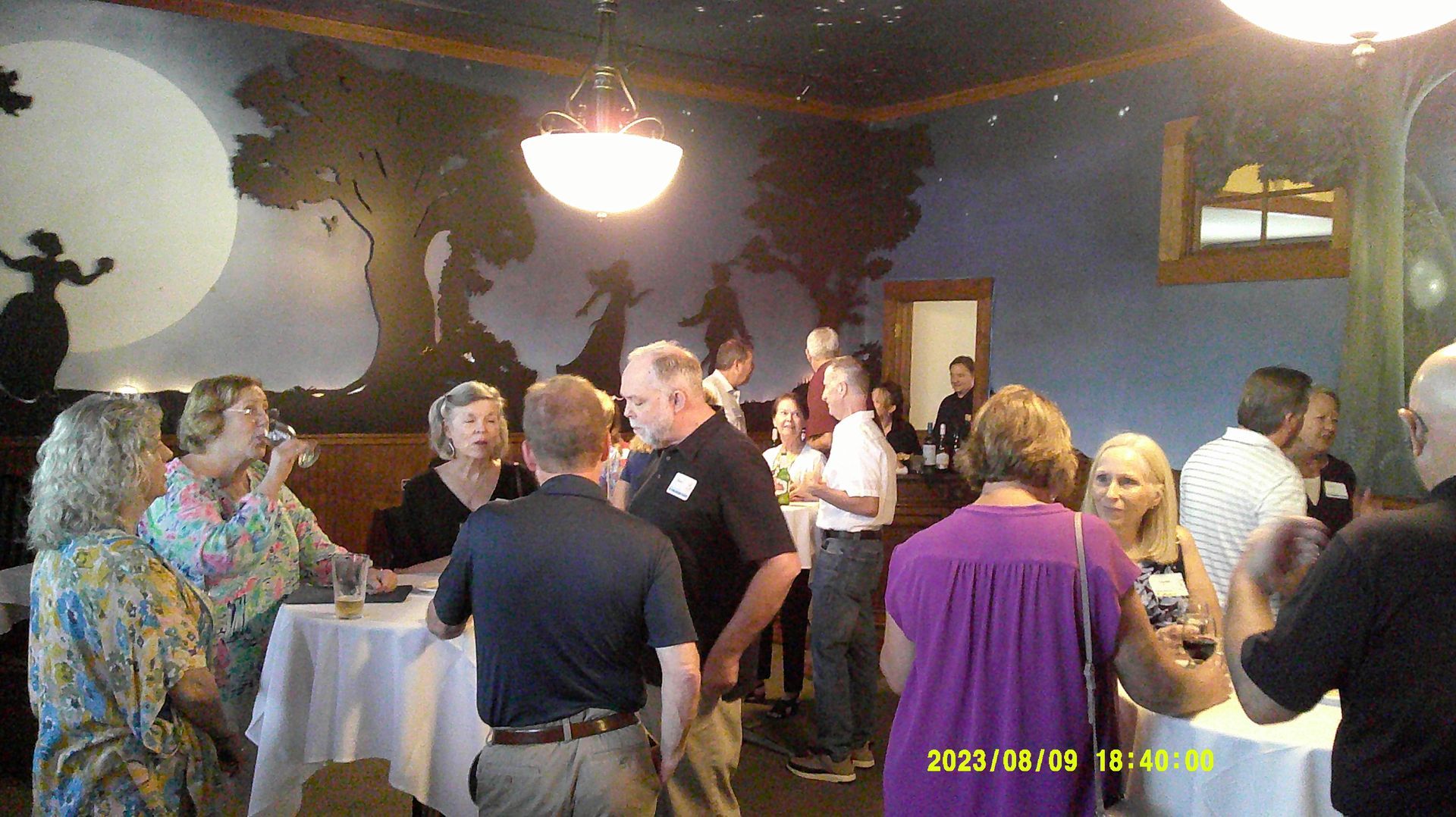A group of people are standing around tables in a room.