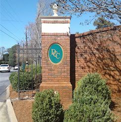 A brick pillar with a green circle on it is in front of a brick wall.