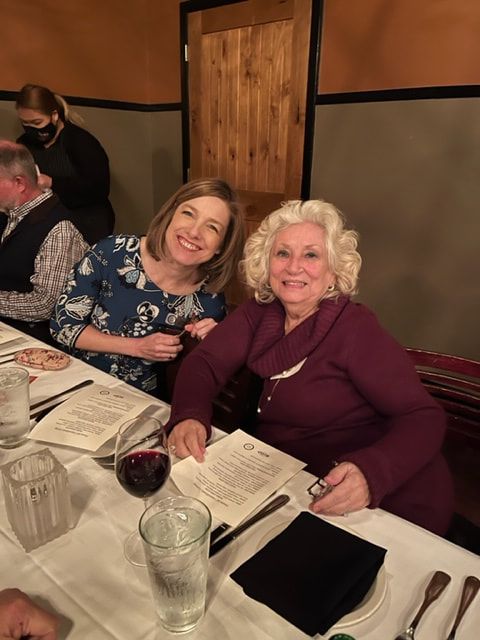 Two women are sitting at a table with a glass of wine.