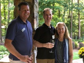 Three people are standing next to each other on a porch holding wine glasses.