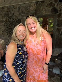 Two women are posing for a picture together in front of a stone wall.