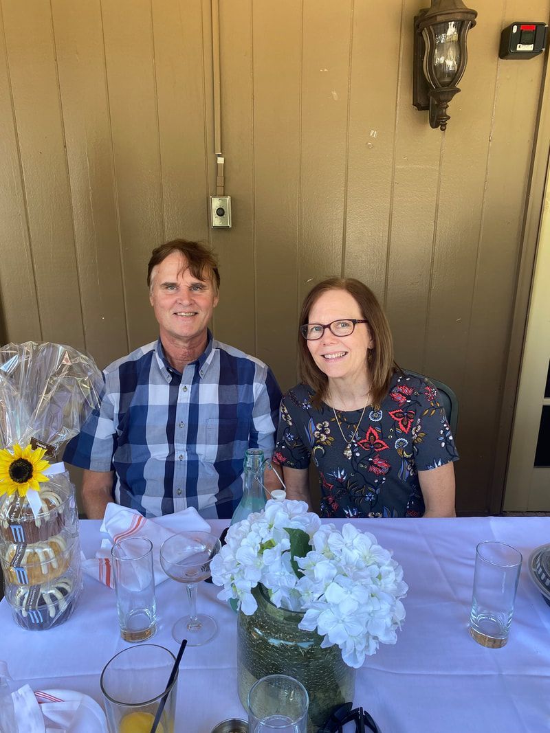 A man and a woman are sitting at a table with flowers in a vase.