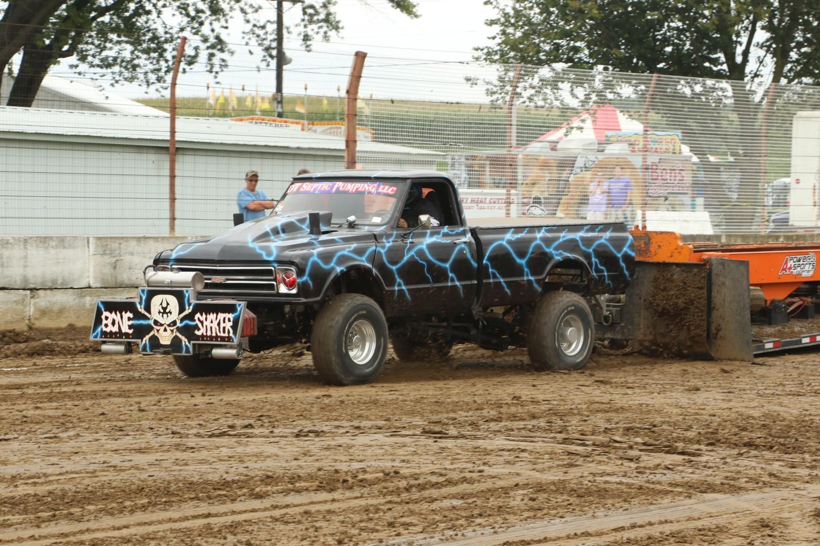 Black truck with blue lightning decals pulling a sled across a muddy dirt track