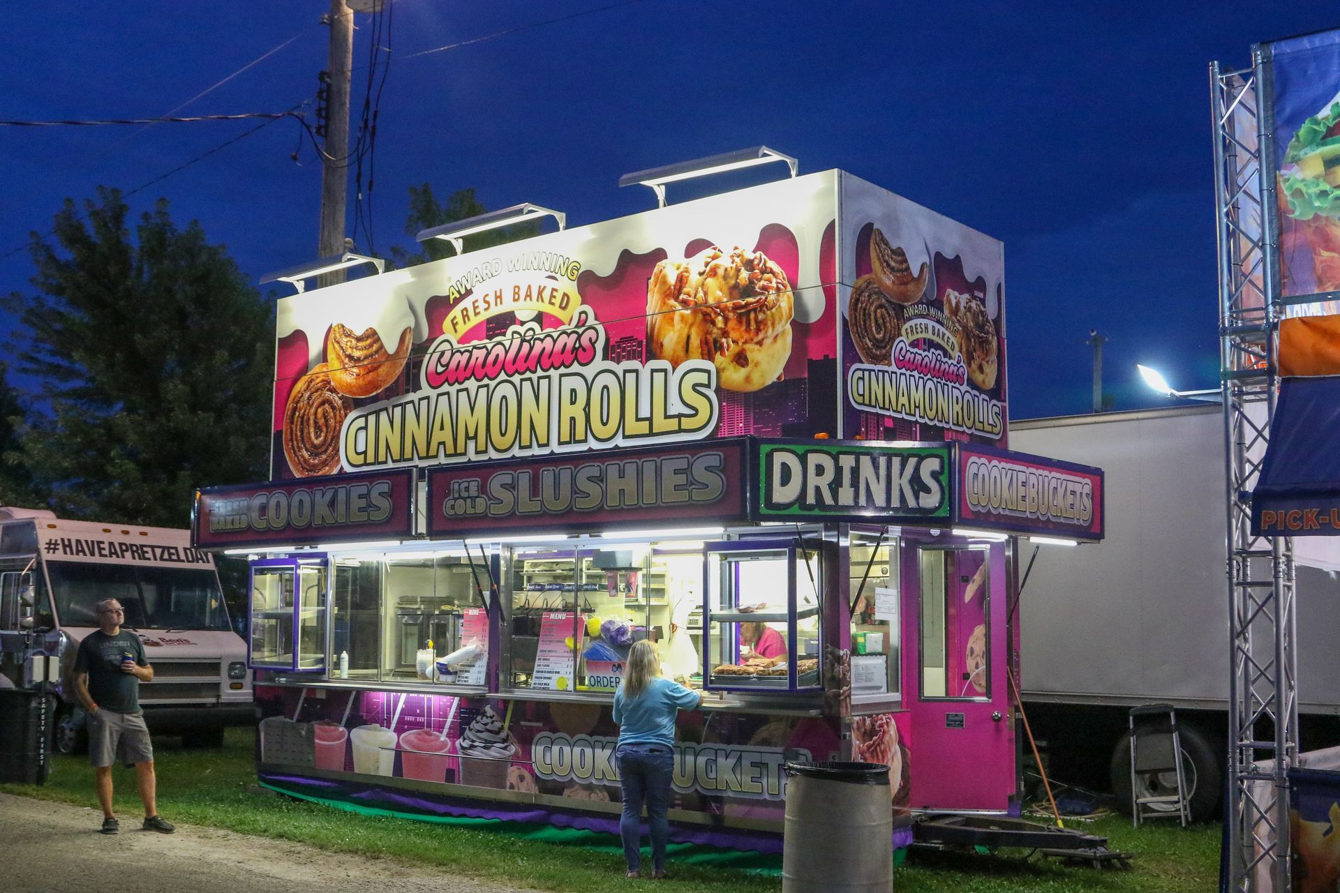 Pink carnival food stand with cinnamon rolls, waffles, and drinks at dusk