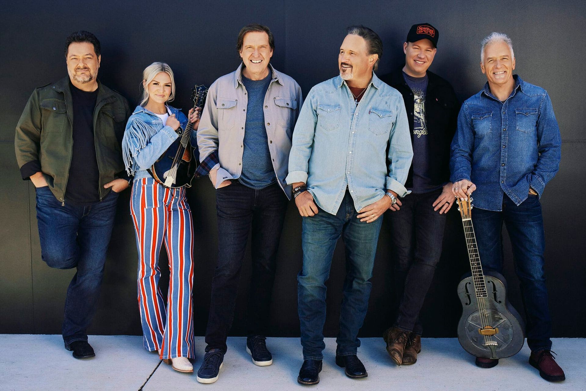 Six people posing against a plain backdrop, smiling in casual clothing.