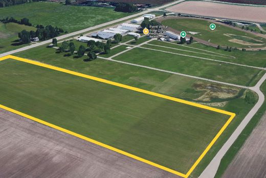 Aerial view of a green field outlined in yellow beside farm buildings and roads.