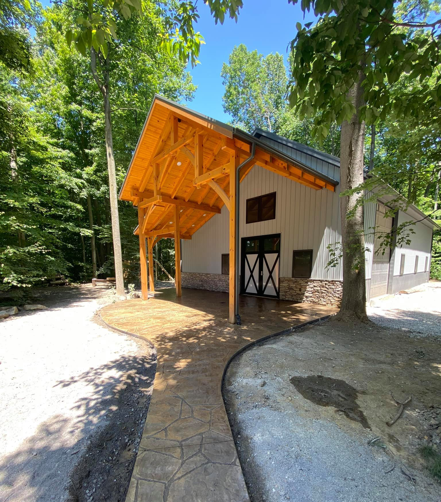 A white barn with a wooden roof is surrounded by trees.