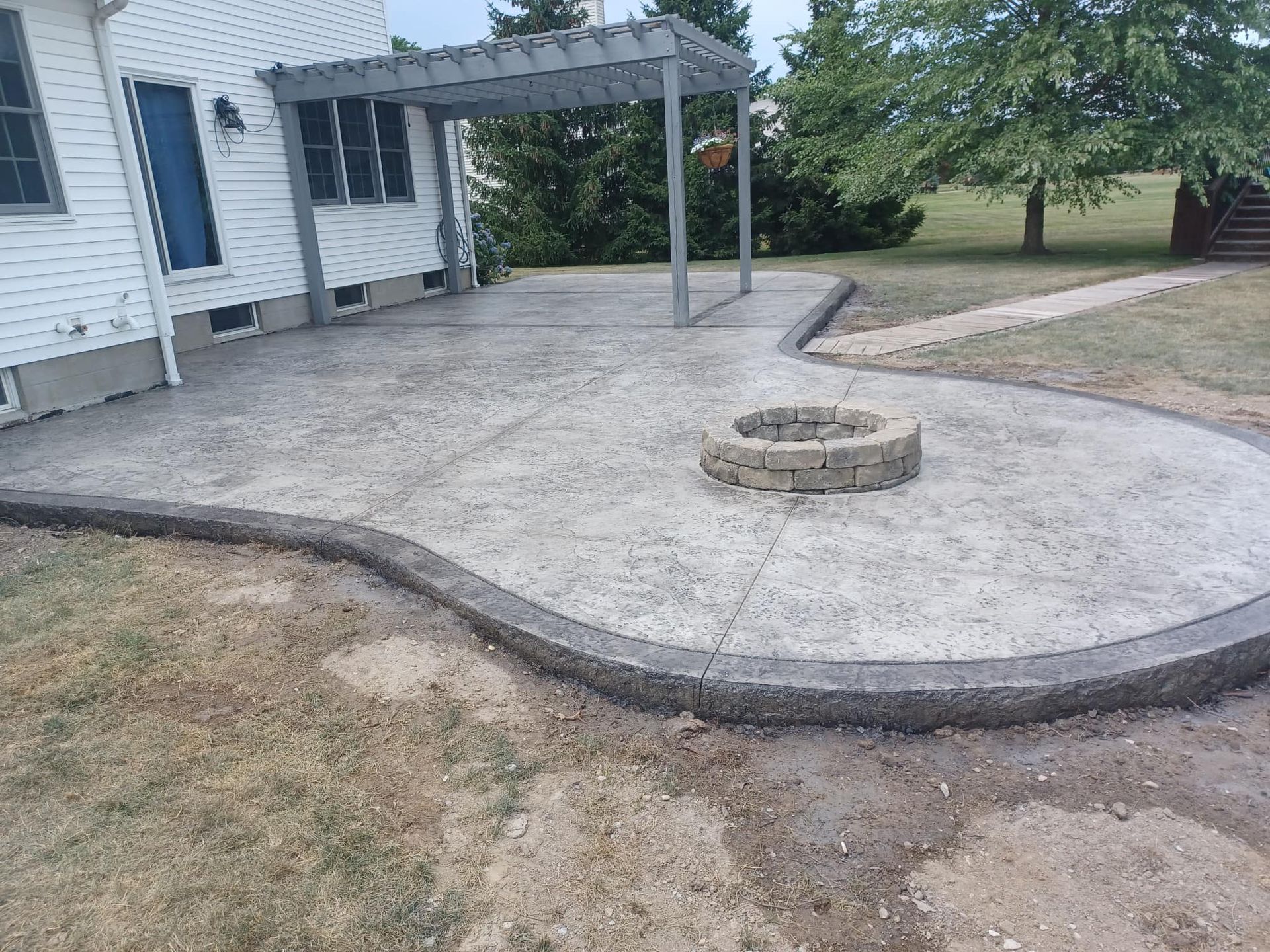 A concrete patio with a fire pit and a pergola.