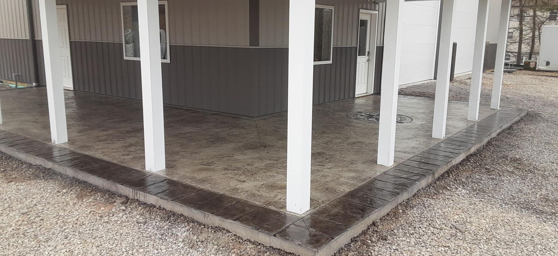 A concrete patio under a porch with white pillars.