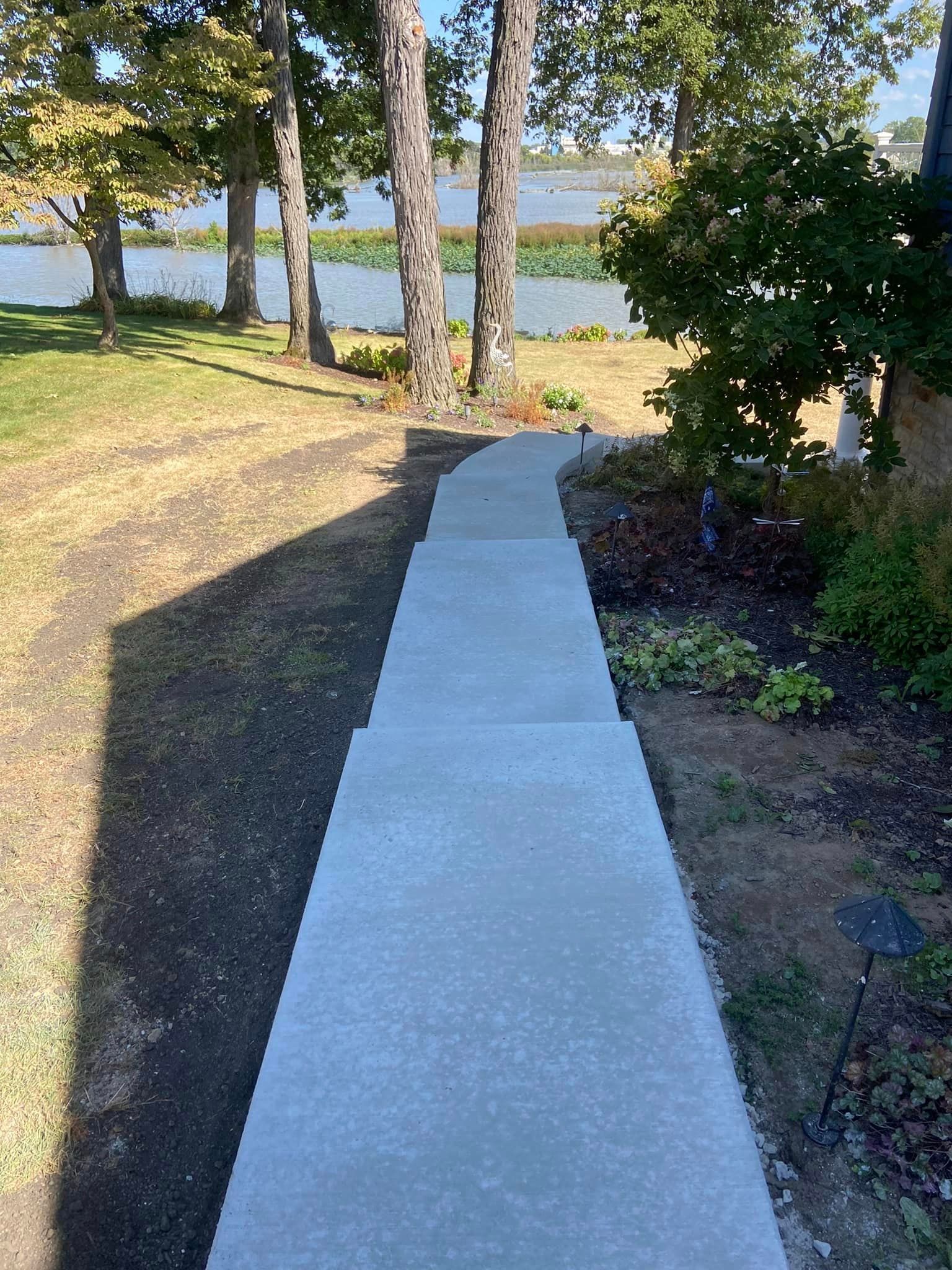 A concrete walkway leading to a lake with trees on both sides.