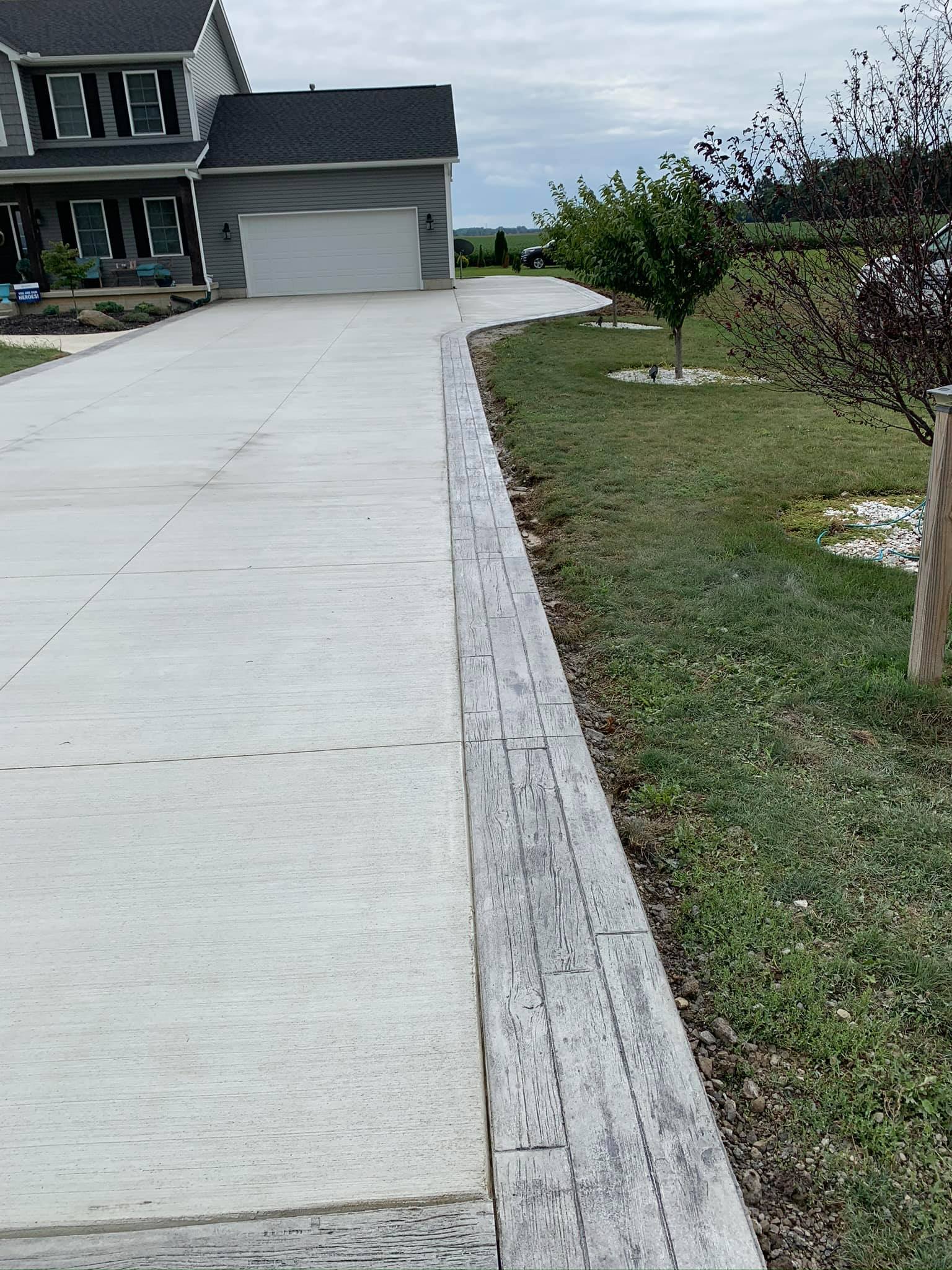A concrete driveway leading to a house with a wooden curb.