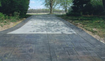 A concrete driveway leading to a field with trees on both sides.