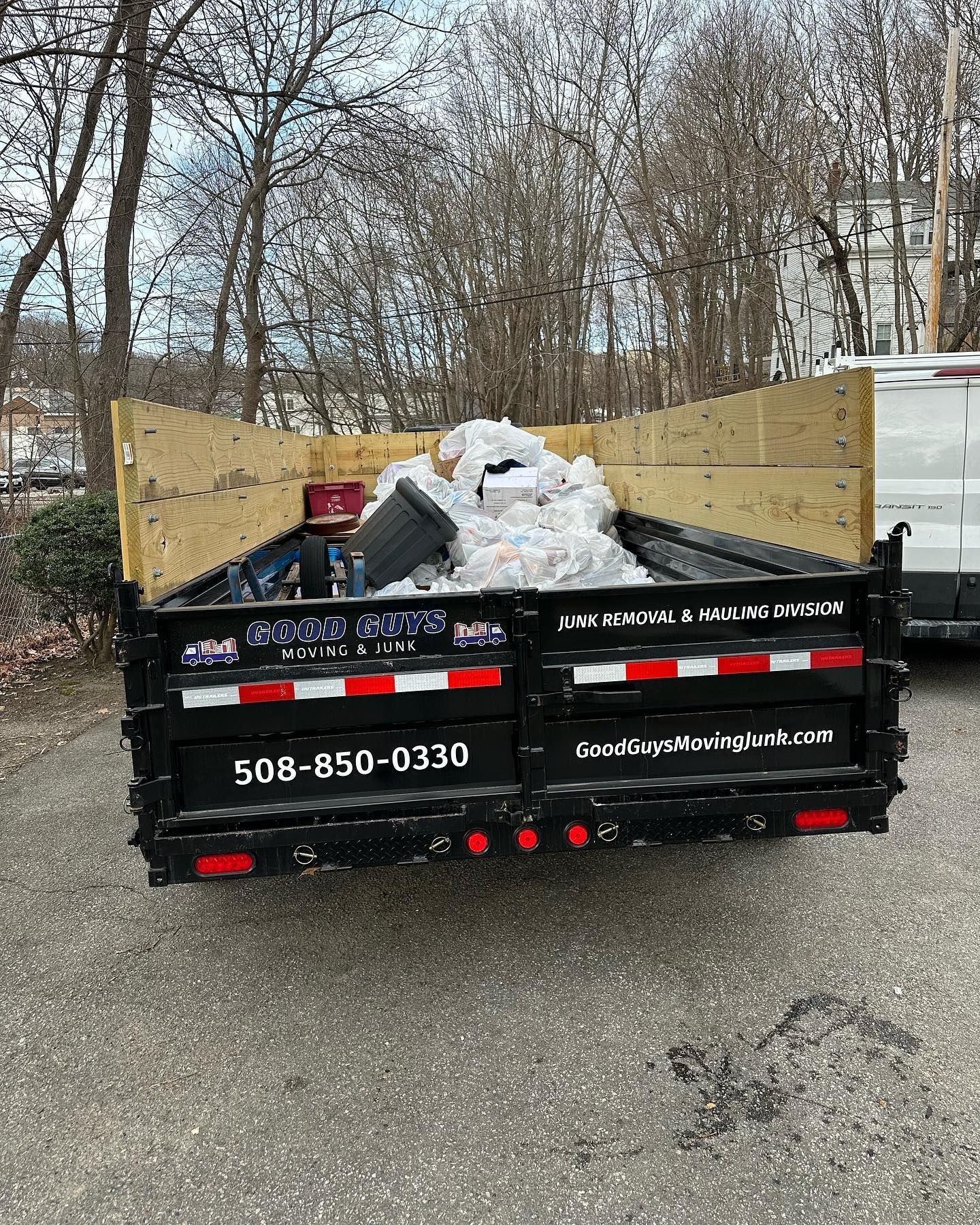Black trailer filled with debris, wooden sides, parked outdoors. Phone number on side: 508-850-0330.