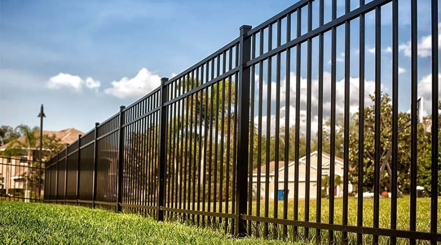 Low-angle view of a modern black aluminum residential fence installed along a green grass lawn under