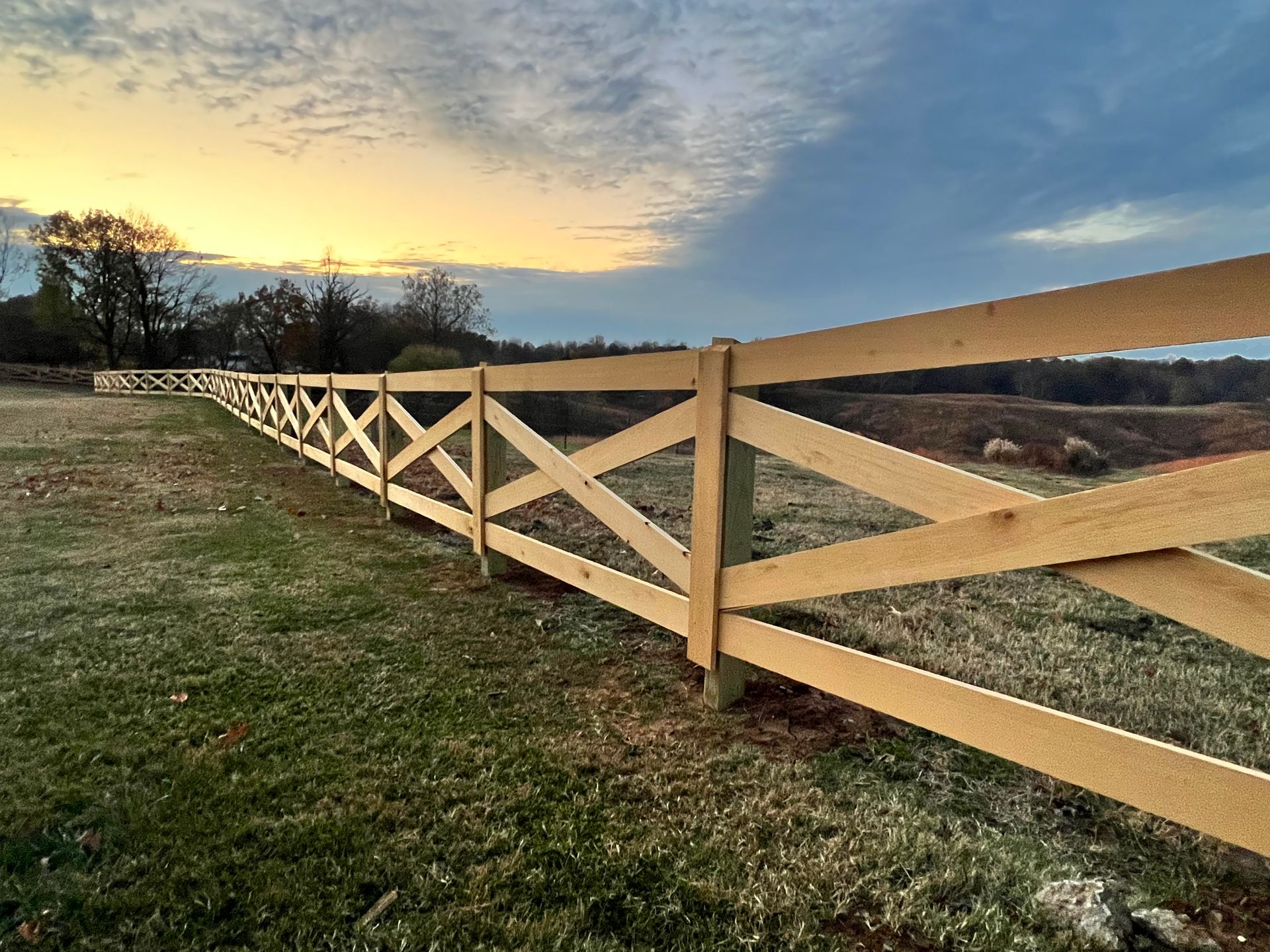 A wooden fence surrounds a grassy field with a sunset in the background.