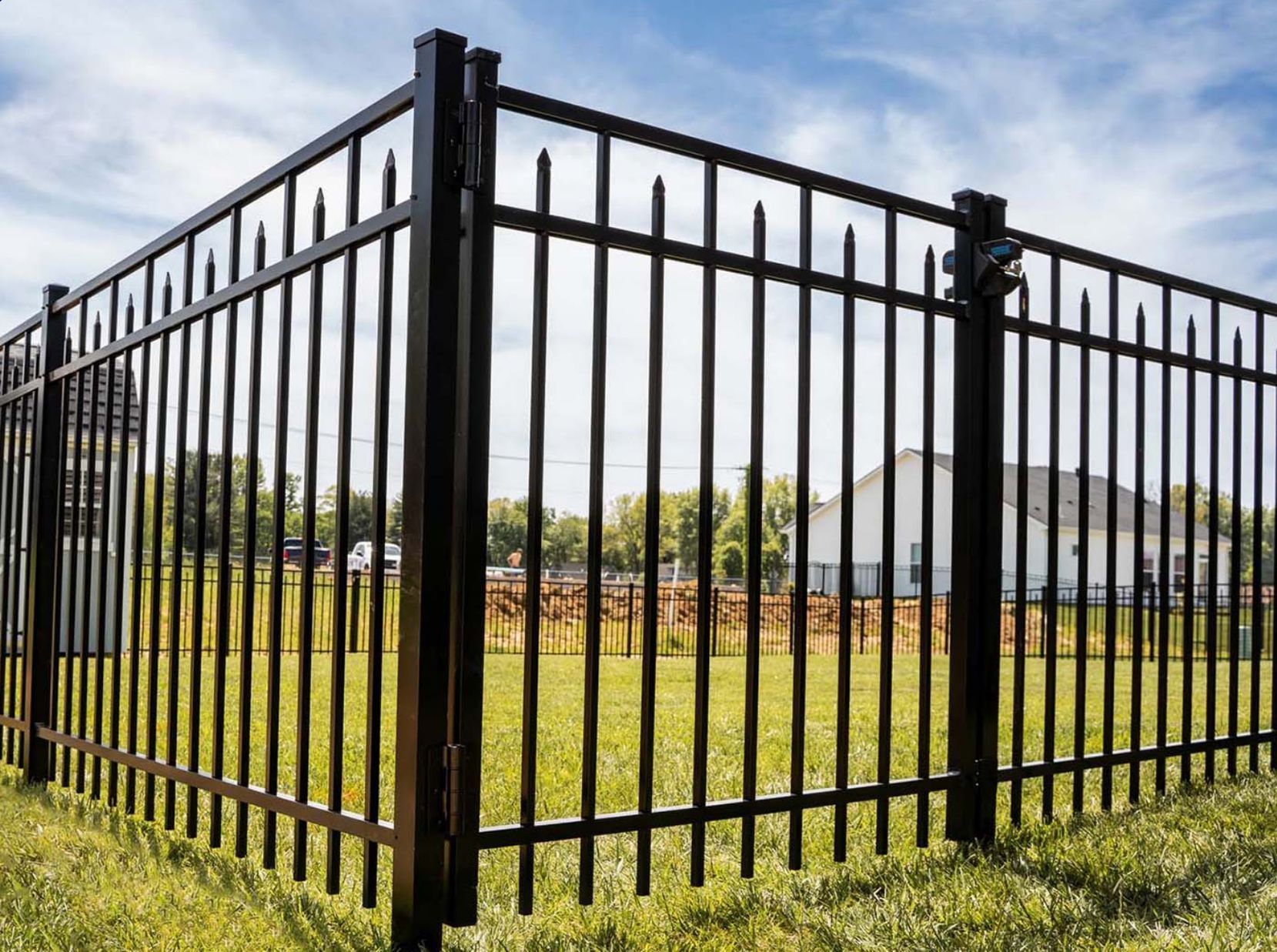A black metal fence is surrounding a grassy field.
