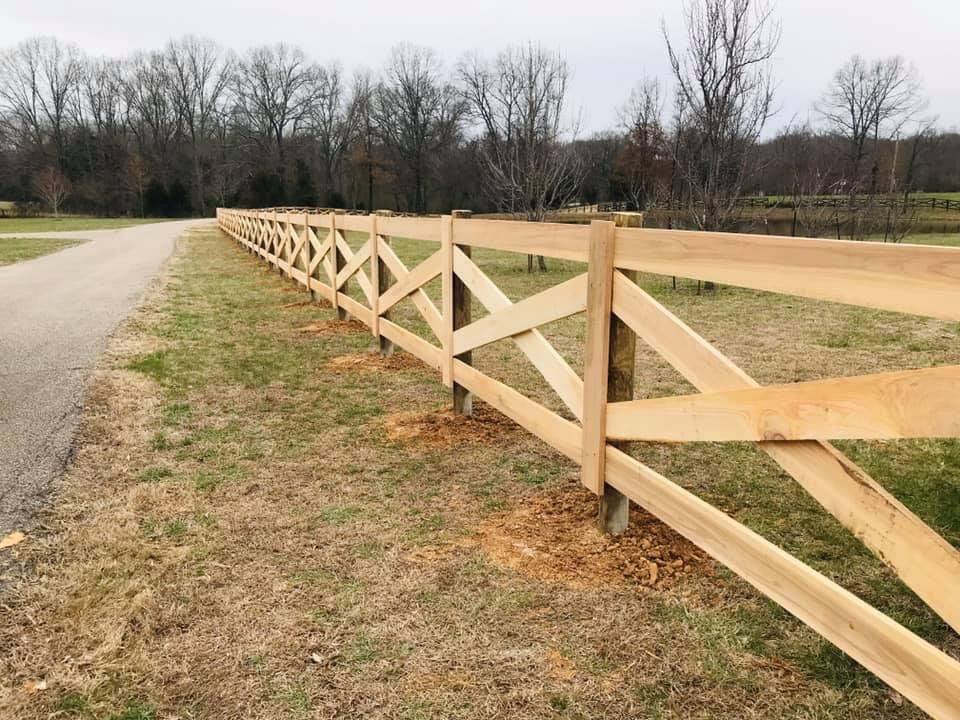 A wooden fence surrounds a grassy field next to a road.