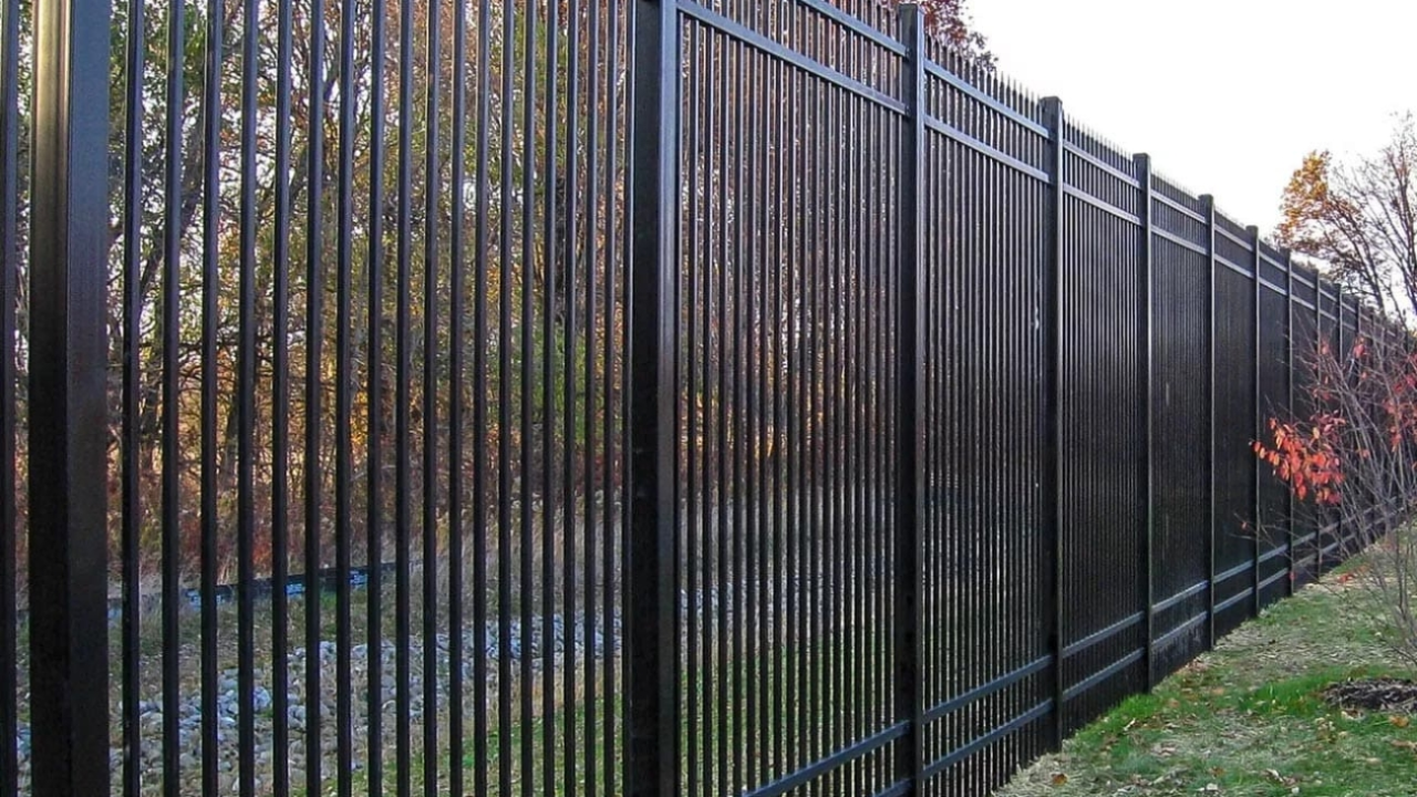 Black metal fence along a grassy slope, with trees in the background.