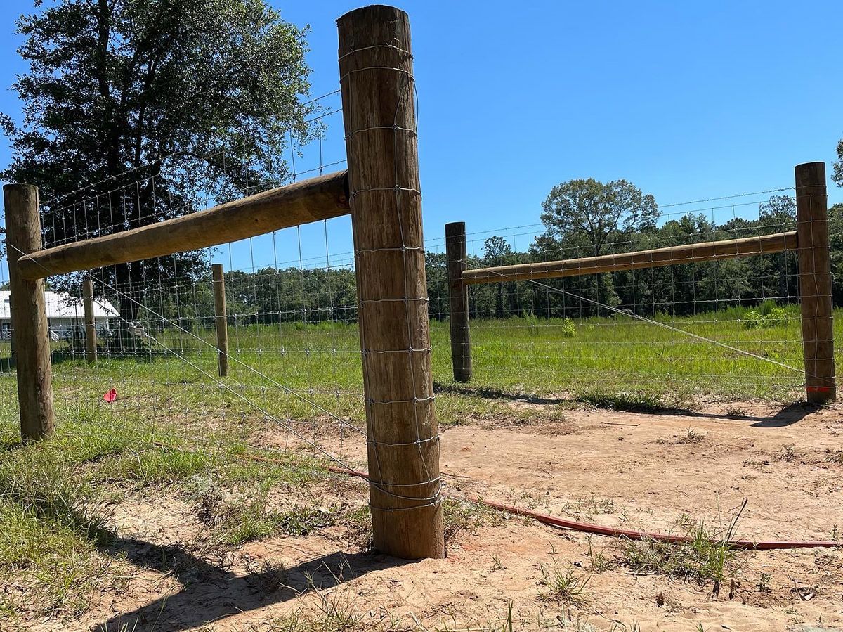 Wooden fence posts and rails stand in a grassy field under a blue sky.
