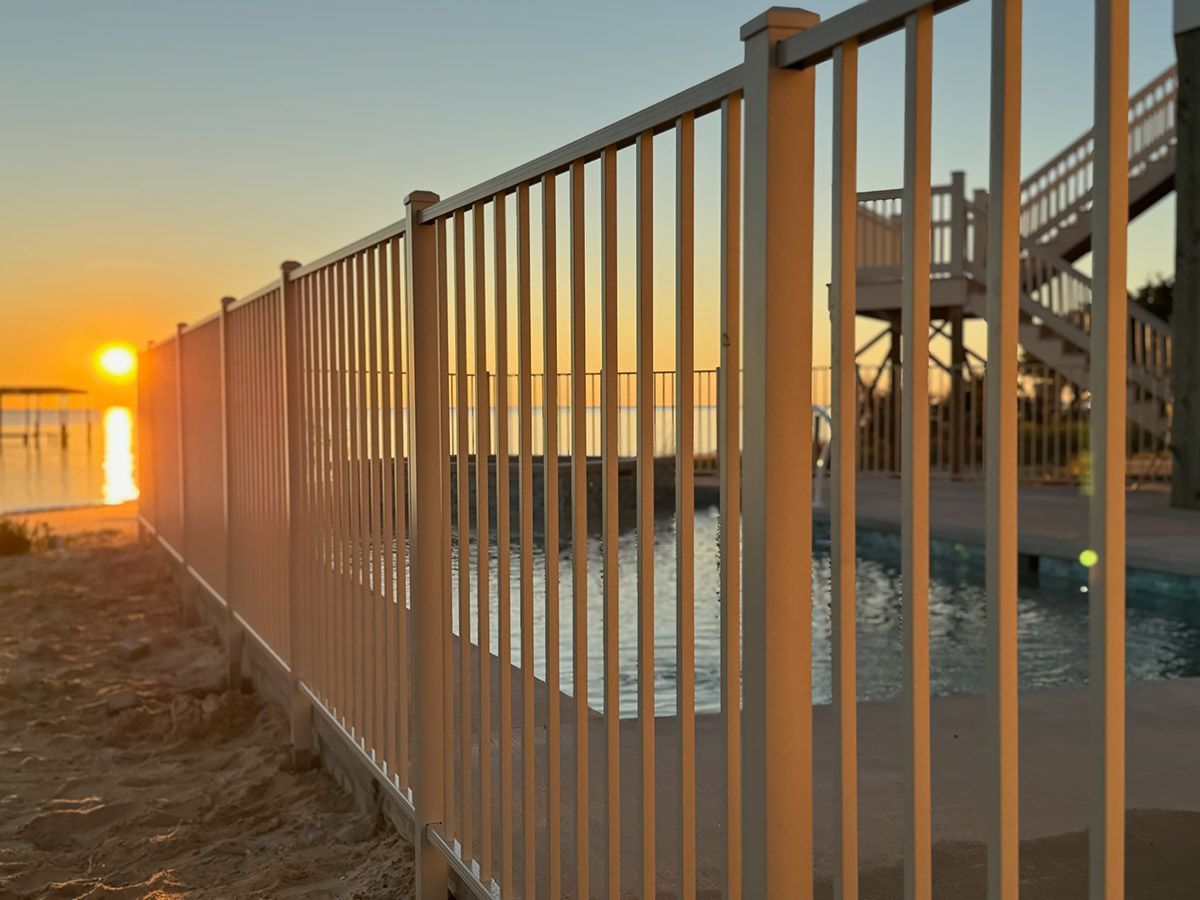 Sunset view through a white fence along water. A pool is on the right.