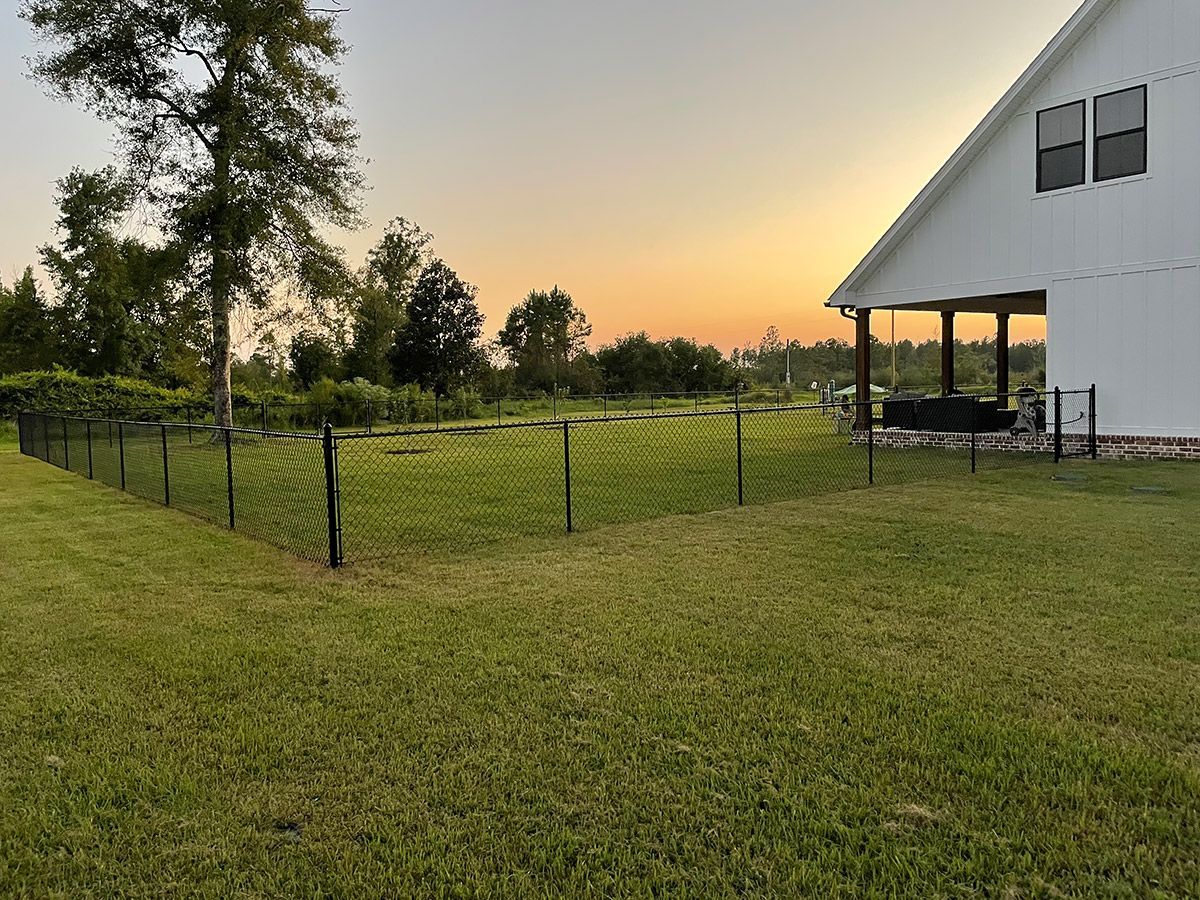 A grassy yard with a black fence, a white house, and a sunset in the background.