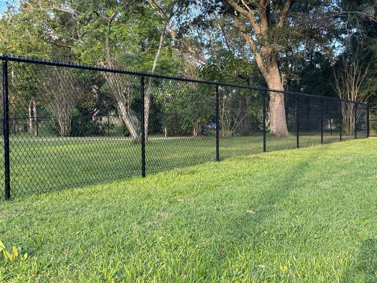 Black chain-link fence in a grassy yard with trees in the background.