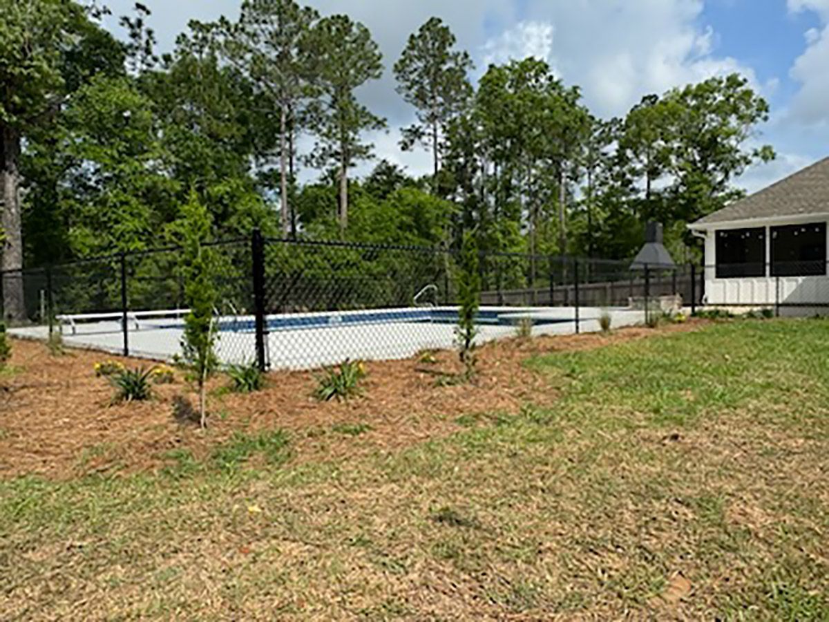Backyard pool surrounded by a black fence, trees, and grass.