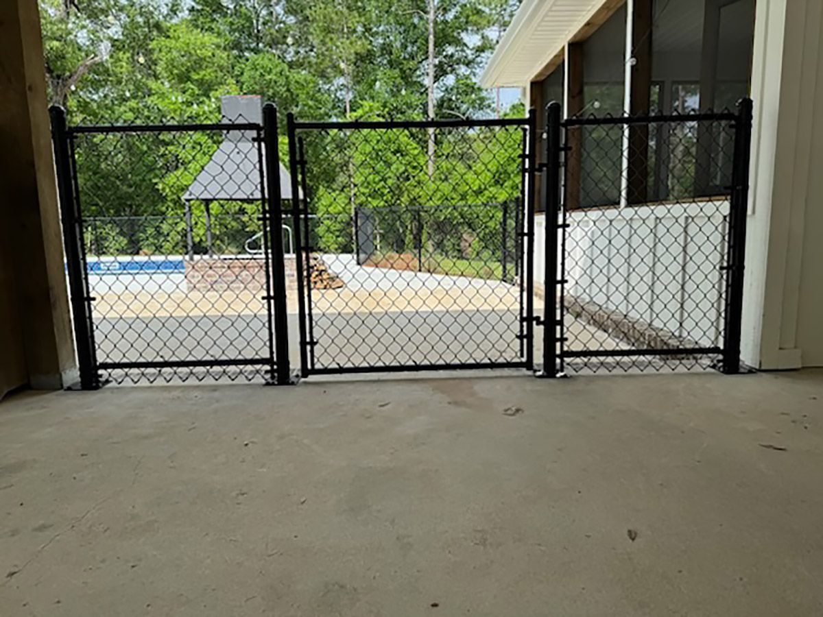 A chain link fence is surrounding a patio with a pool in the background.