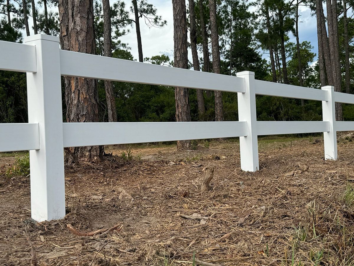 A white fence surrounds a field with trees in the background