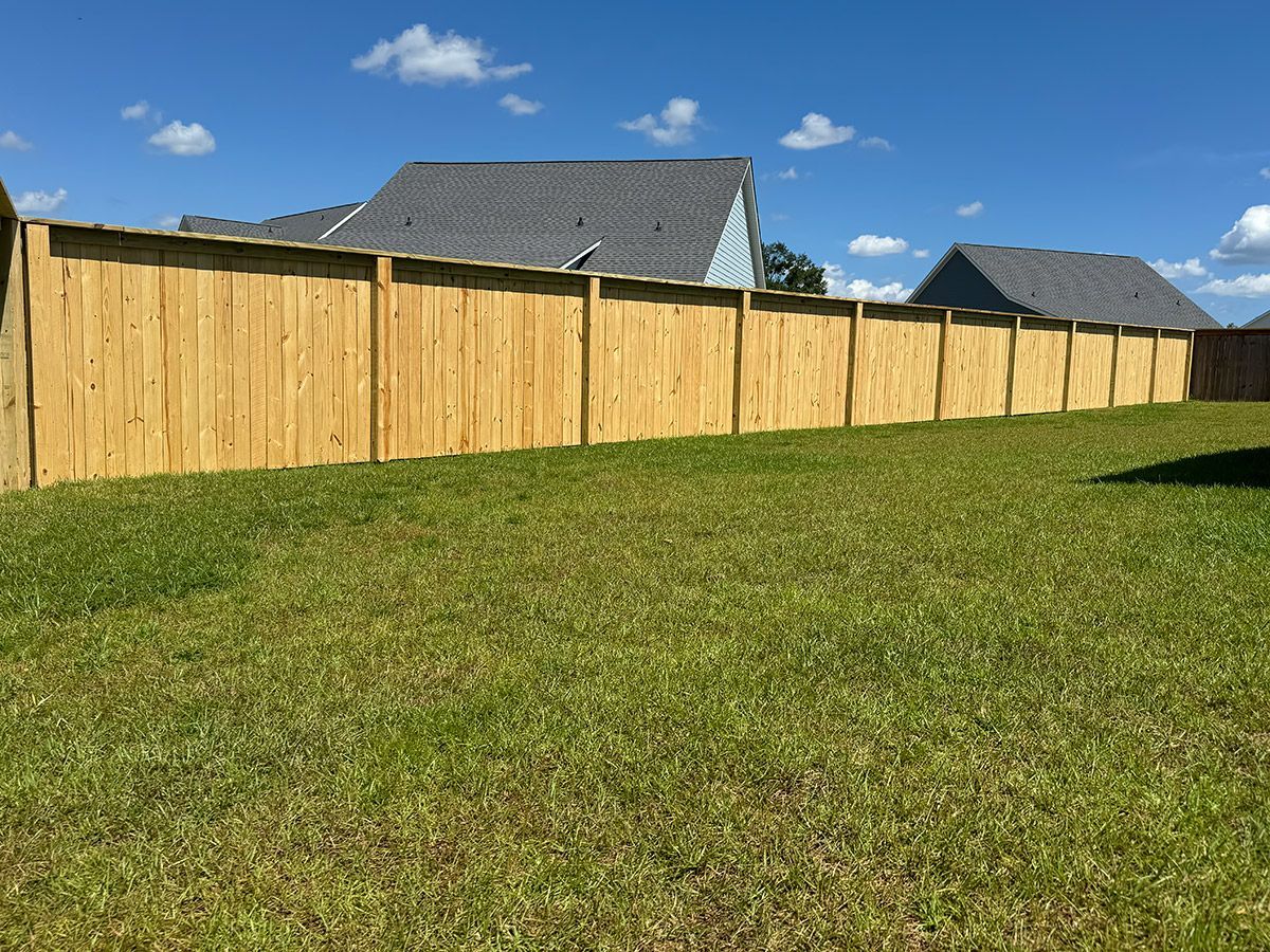 Wooden fence in a grassy backyard on a sunny day, with houses in the background.