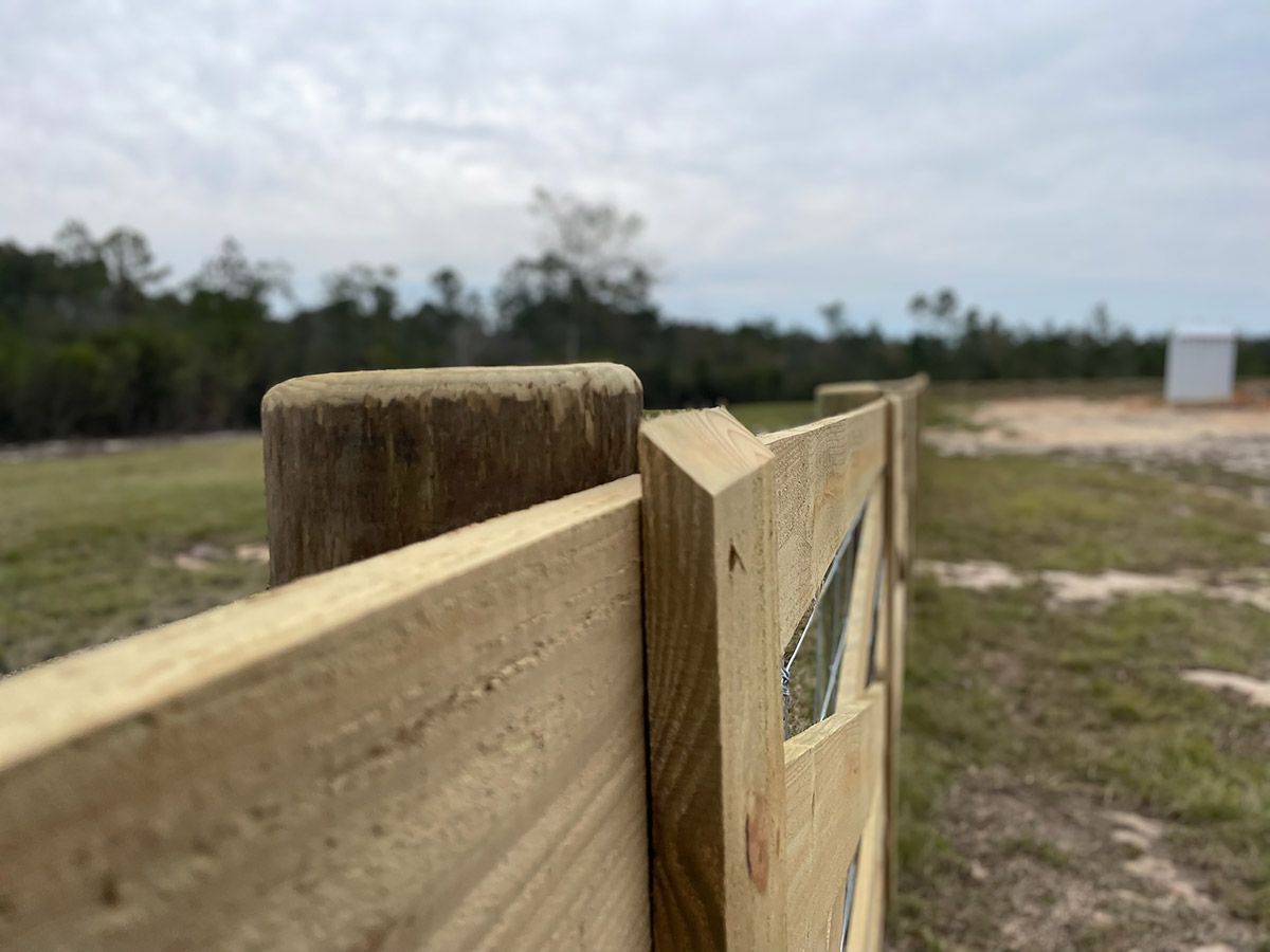Wooden fence in a field, leading into the distance under a cloudy sky.