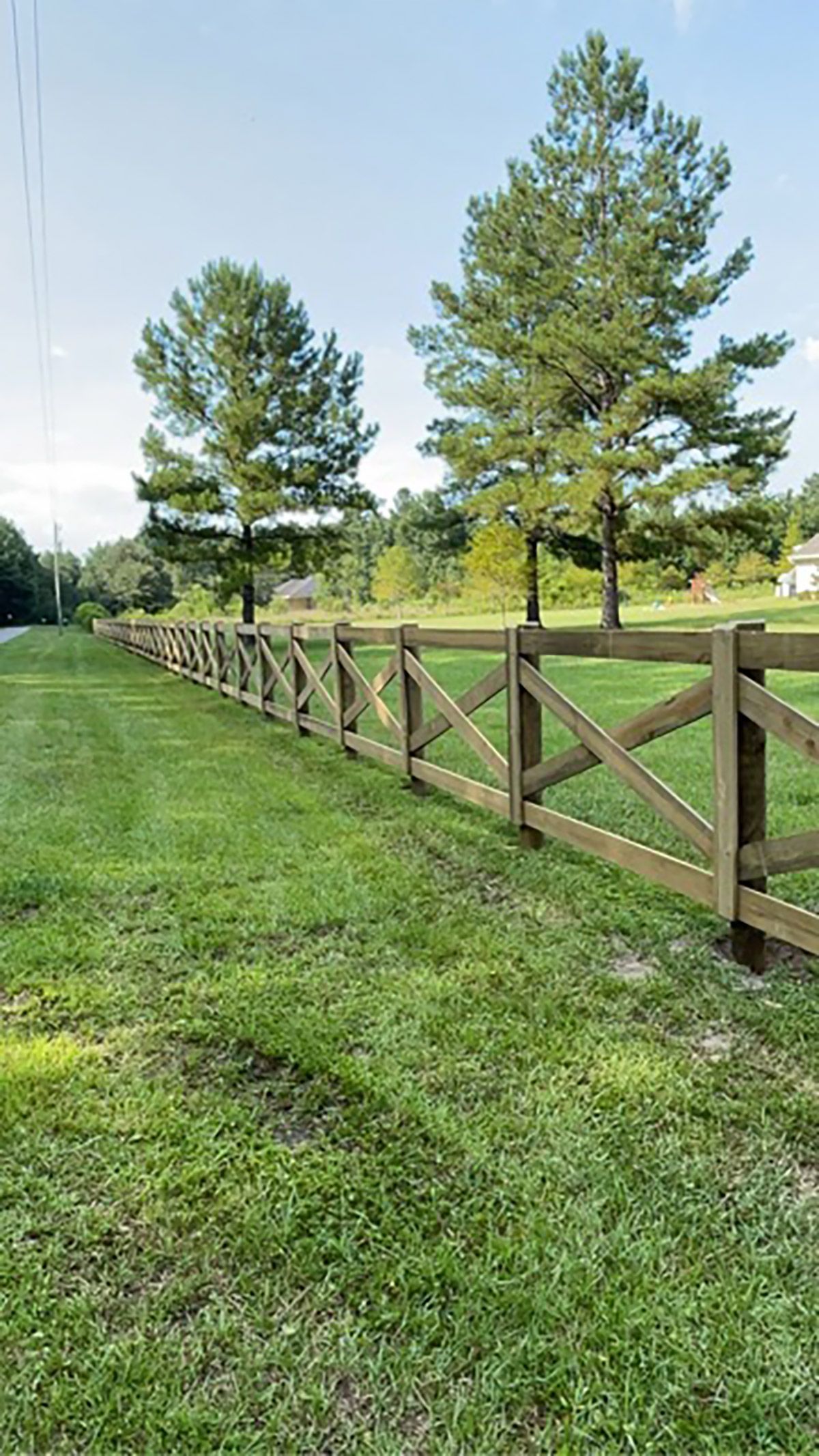 A wooden fence with an X design stretches along a grassy field, with trees in the background.