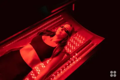 Woman wearing goggles lying on red light therapy bed.