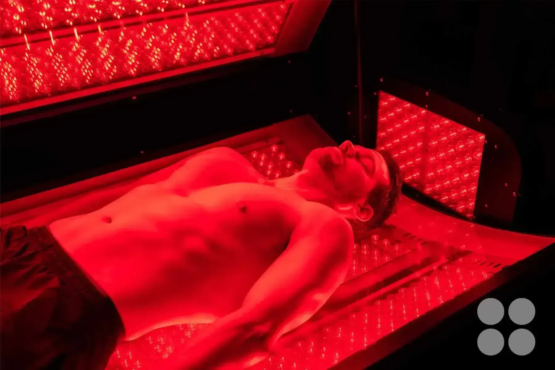 Man lying under red light therapy bed.