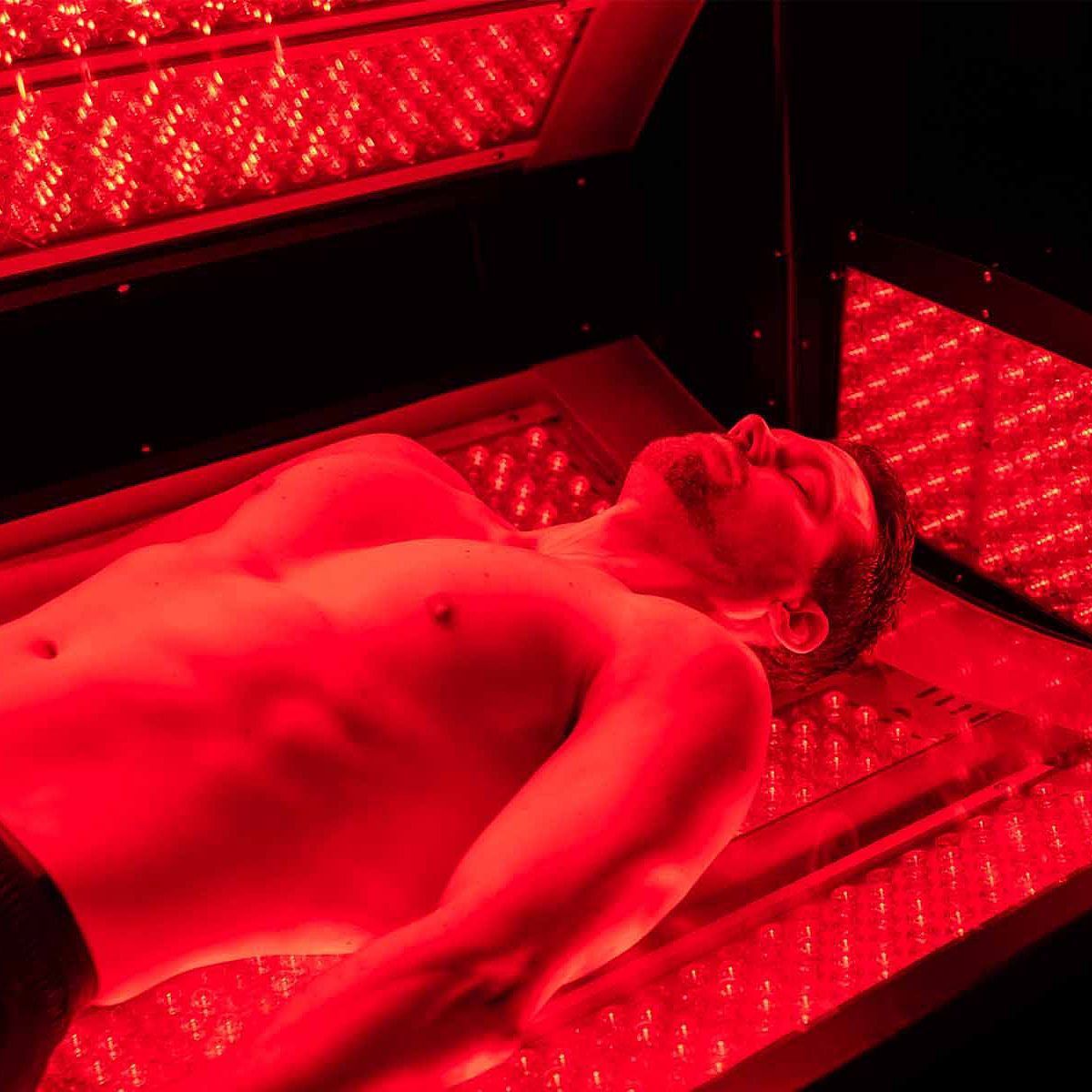 Man lying on a bed under red light panels, receiving red light therapy.