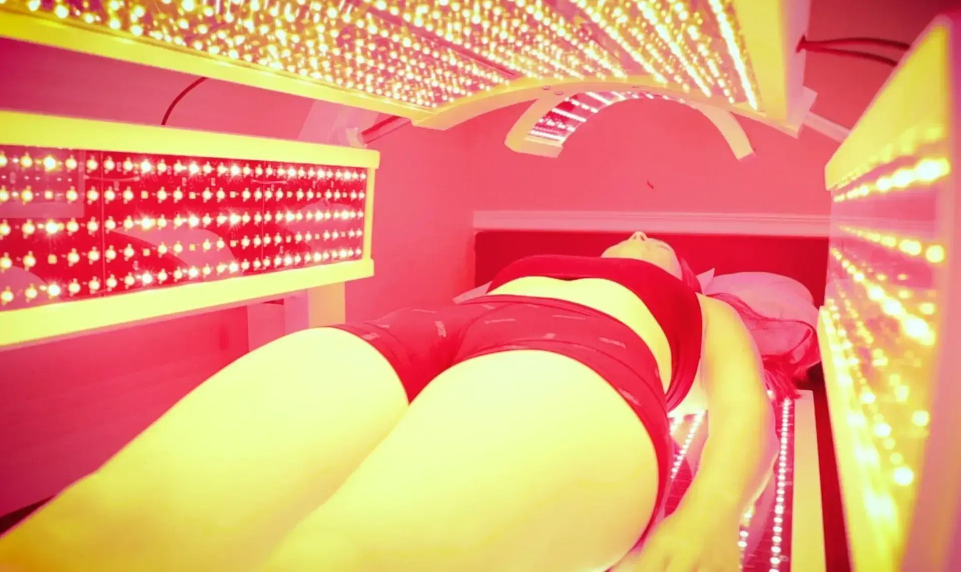 Woman laying in red light therapy bed, illuminated by red LED lights.