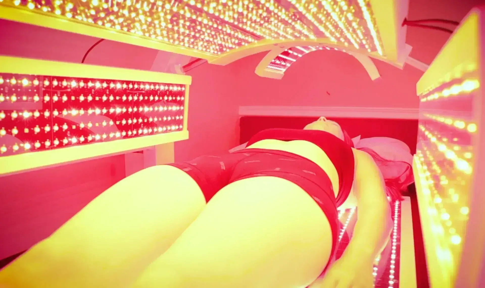 Woman lying in red light therapy bed, illuminated by red LED panels.