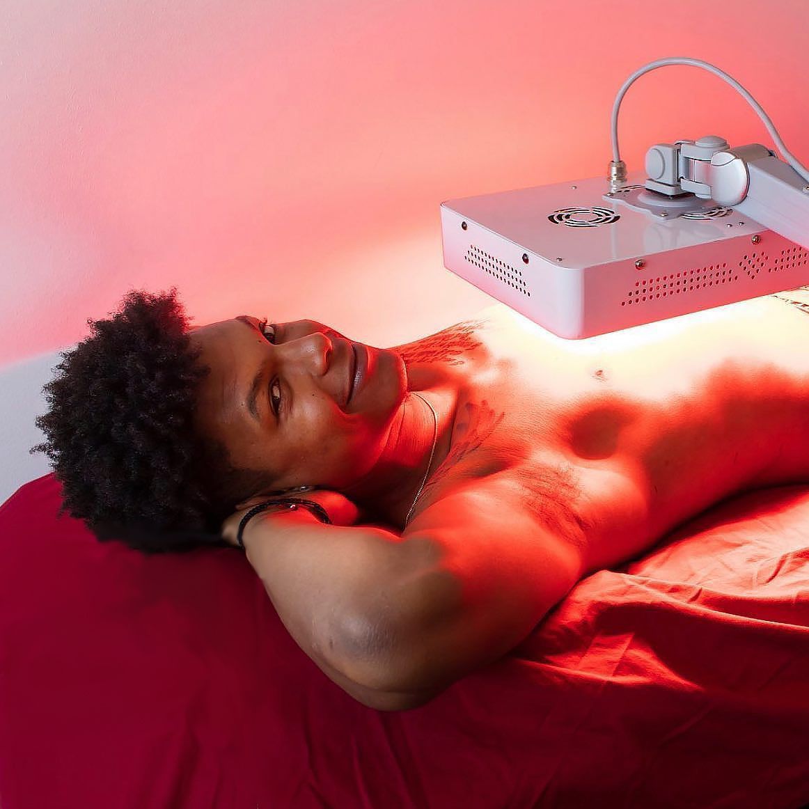 Person receiving red light therapy. Lying on a red surface, red light above.