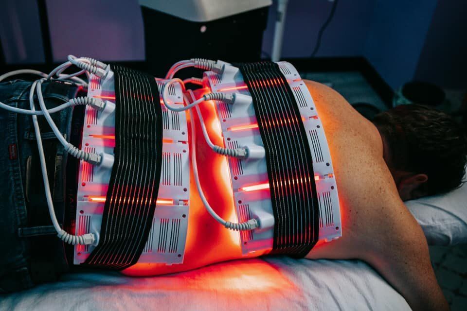 Person receiving red light therapy on their back, lying face down. The device is strapped around the lower back.
