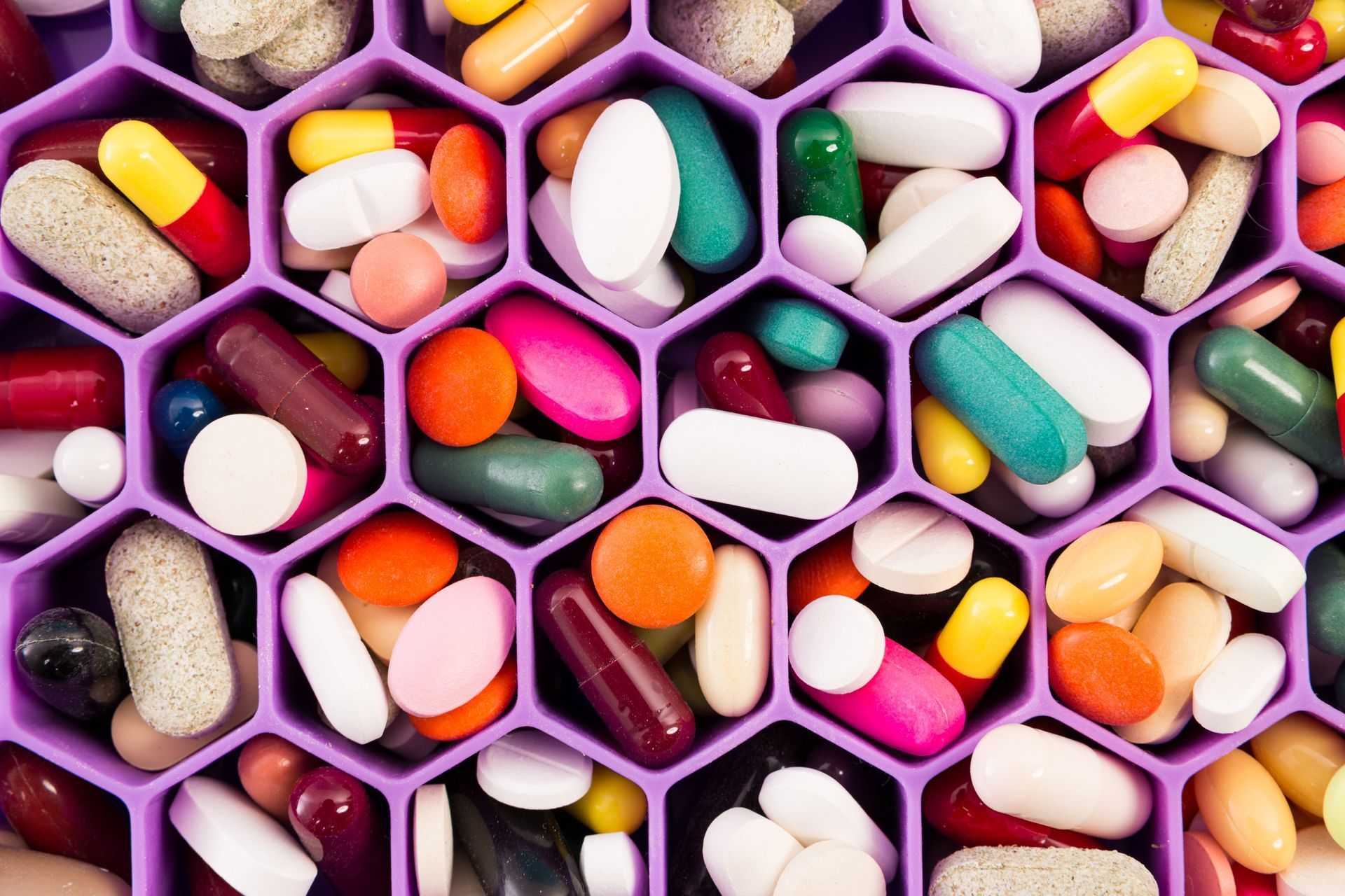 Pills and capsules of various colors filling a purple hexagonal pill organizer.